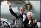 President George W. Bush waves to photographers with Freedom Corps Greeter Lucia Haas in front of Air Force One after his arriving in Phoenix, Arizona, Wednesday, Aug. 11, 2004. Hass, 73, spends two days a week as a volunteer at Surprise Senior Center in Surprise, Arizona, where she teaches English and Spanish Classes, calls Bingo games, instructs needlecraft and sewing classes and serves meals to seniors.  White House photo by Eric Draper
