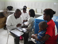 Photo of a researcher interviewing a mother and child, and entering the data into a PDA.