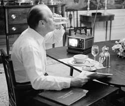 Photo: President Ford sitting at a table with breakfast, small television and documents.