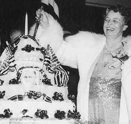 Photo:  Eleanor Roosevelt cutting a very large layer cake decorated with flags an bows.