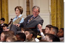 President George W. Bush, sitting with Mrs. Laura Bush, reaches to hold the hand of a young child Monday, Dec. 8, 2008 in the East Room of the White House, during the Children's Hoilday Reception and Performance.  White House photo by Eric Draper