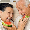 An older man and woman feeding each other watermelon.