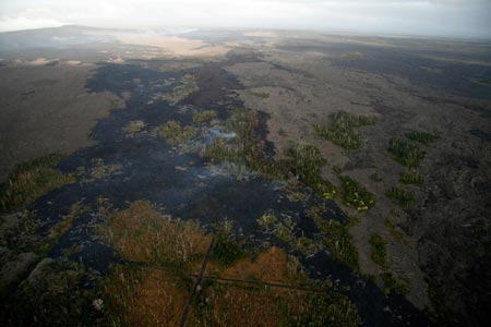 Oblique aerial view of the 4.7 km (2.9 mile) long flow that stalled in its advance toward the Royal Gardens subdivision (still smoking). The intersection of Prince Avenue and Ekaha St. is in the foreground and Pu`u `O`o (left) and the TEB shield (right) are fuming in the background.