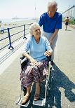 An elderly man pushing his wife in a wheelchair at the beach