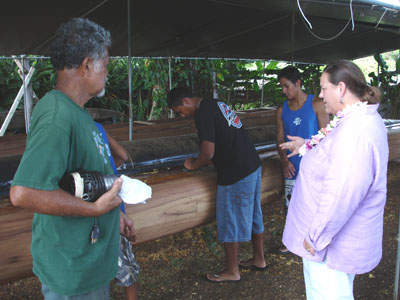 Commissioner Stamps discusses the Healani Canoe Club Restoration and Cultural Preservation project with Uncle Bobby, Master Canoe Builder, while youth participants demonstrate sanding techniques.  