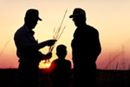 Two men and a child silhouetted in the sunset on a family farm.
