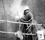 Trabajador en un andamio al lado de un muro de ladrillo, en una nube de polvo