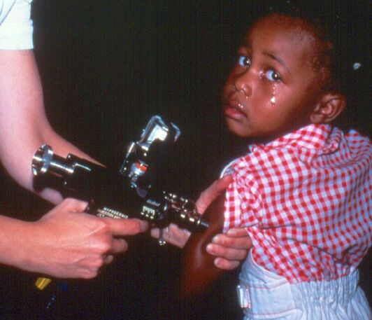 Photo of a teary child being vaccinated using a Ped-O-Jet® needle-free jet injector, circa 1970s.