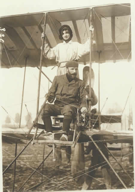 Photo: of a biplane on the ground, with pilot & passenger tied to plane with a  rope.