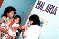 Little girl held by her mother.  A health worker is taking a blood smear from the child.