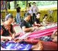 Mrs. Laura Bush and daughter Ms. Barbara Bush try on shawls created by weavers carrying on the traditional Karen ethnic craft at the Mae La Refugee Camp at Mae Sot, Thailand. In her August 7, 2008 comments, Mrs. Bush pointed out that the weavings are done to help generate money for the refugees and can be purchased via the Internet through consortiums that work with women at the camp. The camp houses at least 39,000 refugees waiting for a safe time to return to their home country. Many have decided the wait of 20 years has been too long and have immigrated to the United States and other countries. White House photo by Shealah Craighead