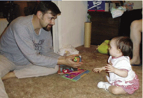 photo of a man and a child; the man is reaching out with a toy