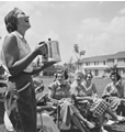 Woman holding coffee pot standing next to group of women neighbors seated in lawn chairs, Park Forest, Illinois