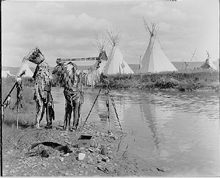 Two Native Americans, wearing feather headdresses, looking at photographic film