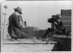 Two photographers taking each others' picture with hand-held cameras while perched on roof, LC-USZ62-97707