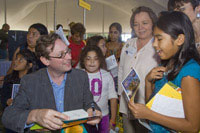 A man signing a book while a group of women and girls look on.