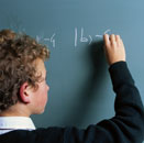 Image of a school age boy doing a mathematics calculation at a chalkboard