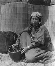 Woman kneeling on the ground , using a  mortar and  pestle.