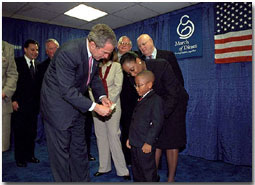 After presenting President George Bush with a pair of boots, March of Dimes Ambassador Justin Lamar Washington gives the President a dollar to help with contributions to the Afghan children during the organizations' Washington D. C. event Oct. 12. White House photo by Tina Hager.