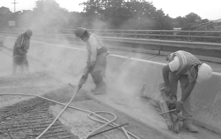 Workers on a roadway construction site in a thick cloud of dust