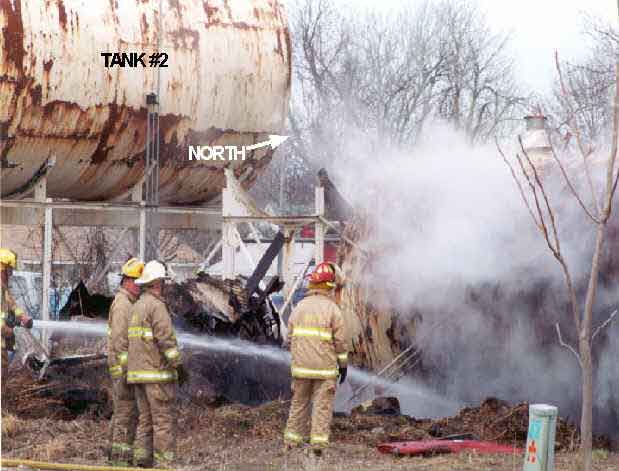 Photo 2: Photograph of the south side of Tank #1 prior to the explosion, showing fire fighters applying water to the tank’s surface.
