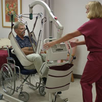 Nurse with mechanical lift transfering a man to a wheelchair