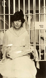 A woman sitting near the bars of a prison cell.