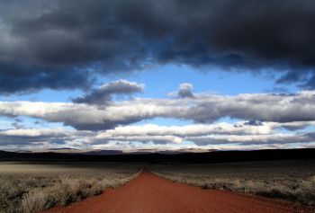 Blue sky with white clouds against the red gravel of the Barrel Springs Backcountry Byway.  Photo taken by Laurie Sada