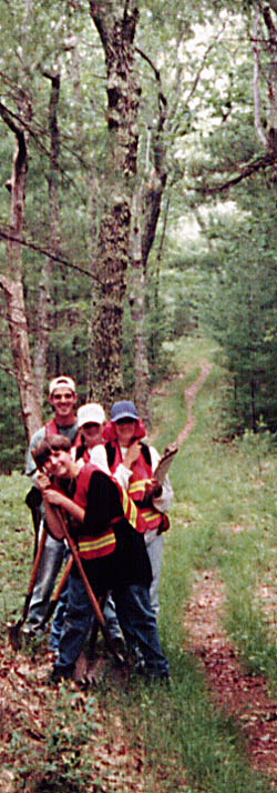 [NPS photo] Four kids with archeology equipment pose on a wooded path.