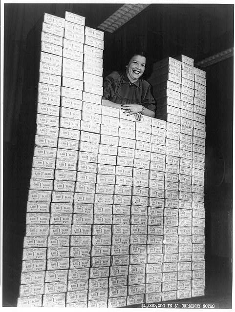  Woman posed with stack of packages of $1 silver certificates at the Bureau of Engraving and Printing, Washington, D.C. [between ca. 1950 and ca. 1969]