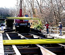 Photo: a small crane lifting large fiberglass planks into place on a bridge.