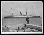 A figure on the dock looking at an ocean liner