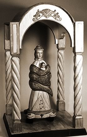 Photo of a small carved and painted wooden figure, sheltered by an arch held up by columns.  The image is of the Virgin Mary with her child.