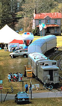 Brids-eye view of a train with the town in the background.  A tent and a hot air ballon can be seen nearby.