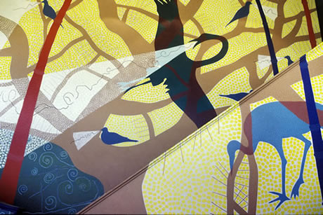   Detail of a mural. Two large blue cranes, one in flight, one standing with head down, are depicted layered over a network of sinuous brown branches, which are layered over a white ground speckled with yellow dots of varying density				