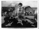 Black woman working with flag spread out

in front of her, piles of folded fabric behind her