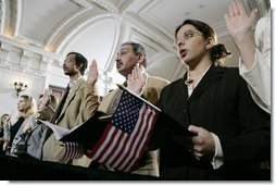 Naturalization ceremony participants raise their hands and hold American flags as they are sworn-in as new U.S. citizens Monday, March 27, 2006, during the Naturalization Ceremony at the Daughters of the American Revolution Administration Building in Washington. President George W.Bush addressed the audience, saying that each generation of immigrants brings a renewal to our national character and adds vitality to our culture. White House photo by Eric Draper