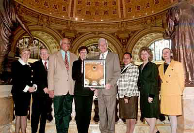 Director of Congressional Relations Geraldine Otremba; John Cole, director of the Center for the Book; Deputy Librarian Donald Scott; Ethel Kessler, the stamp's designer; Dr. Billington, Chief of Staff Jo Ann Jenkins; Roberta Stevens, Bicentennial program manager; and Public Affairs Officer Jill Brett stand on the balcony of the Main Reading Room, whose dome is seen in the Library of Congress commemorative stamp.