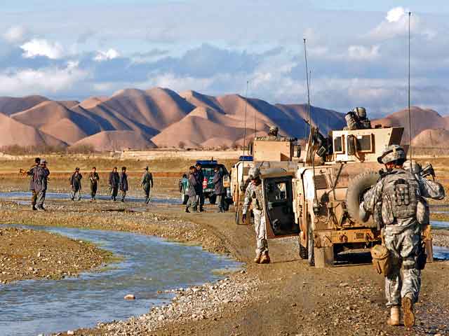 This photo shows several members of the Coalition forces and local police exiting military vehicles to begin a patrol.  They are walking along a stream and an Afghanistan mountainside is in the background.