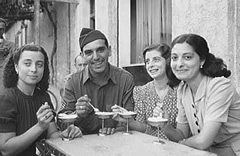 Soldier and three women eating ice cream at sidewalk cafe.