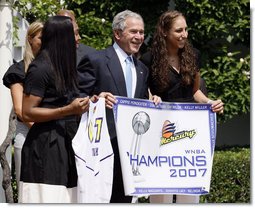 President George W. Bush, joined by Diana Taurasi, left, and Cappie Pondexter, is presented a Phoenix Mercury Championship banner and a personalized team jersey Monday, June 23, 2008, during the 2007 WNBA Champions, the Phoenix Mercury, visit to the White House. White House photo by Eric Draper