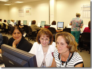 A photo of 3 women looking at a computer monitor while in a training class.