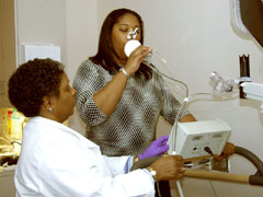Photo of a patient with pulmonary equipment on her nose and mouth and a technician assisting her.