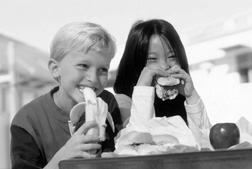 Photo of boy and girl eating their bag lunches.