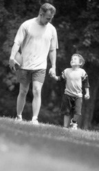 Photo of father and son holding hands, walking in the park.