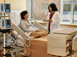 A patient in bed is taught about testing by a staff member