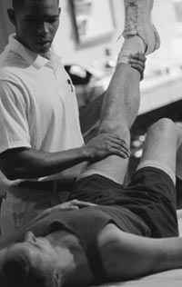 Photo of male physical therapist helping man stretch his legs.