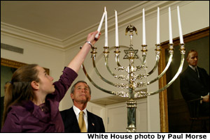 President George W. Bush watches as Daniella Wald, 12, lights one of the candles on the Menorah Wednesday, Dec 4 in the White House. President Bush presented one of the lighted candles to Daniella Wald, who lit the first three candles, and she presented the lighter candle to her sister, Alexandra Wald, 15, who lit the other three. Both of the girls are from Manhattan, and their father, Victor Wald, was killed in the Sept. 11 attacks on the World Trade Center. White House photo by Paul Morse.