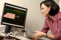 Photo of Allison Okamura demonstrating a haptic deivce that interacts with a virtual environement to display cutting forces to the user.