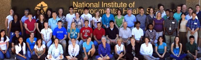 Summers of Discovery interns and mentors collected in front of the Rall Building for their group photo. Coordinator Charle League is shown in blue sitting in the center of the front row.